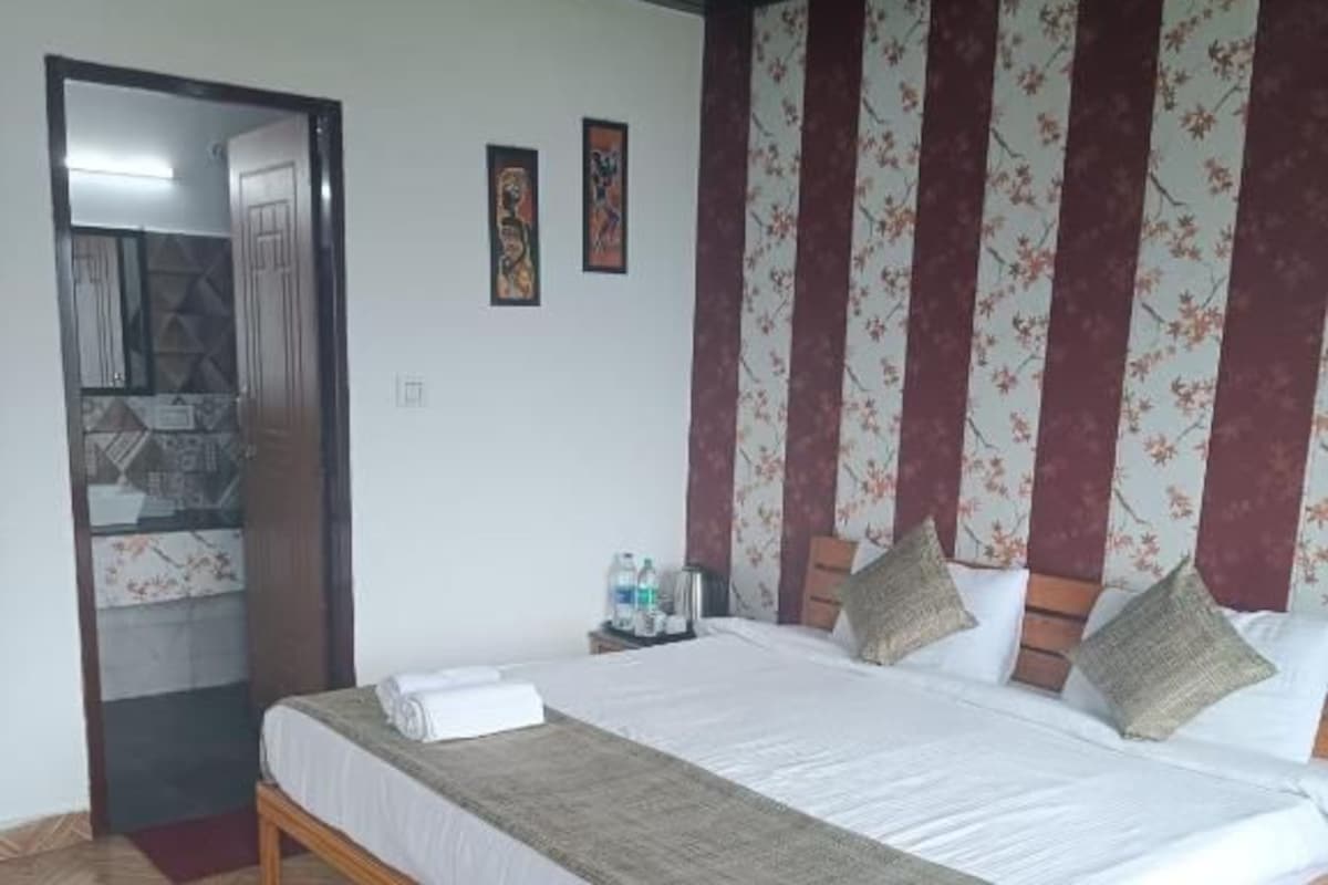A bedroom with a wooden bed, a dark rug, a wooden bench, and a door leading to another room.