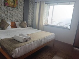 A bedroom with a bed, pillows, a blanket, a window with a view, and a painting on the wall.