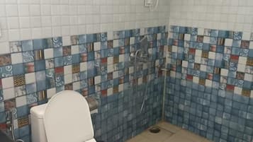 A bathroom with a toilet, a shower, and a tiled wall with a patterned design.