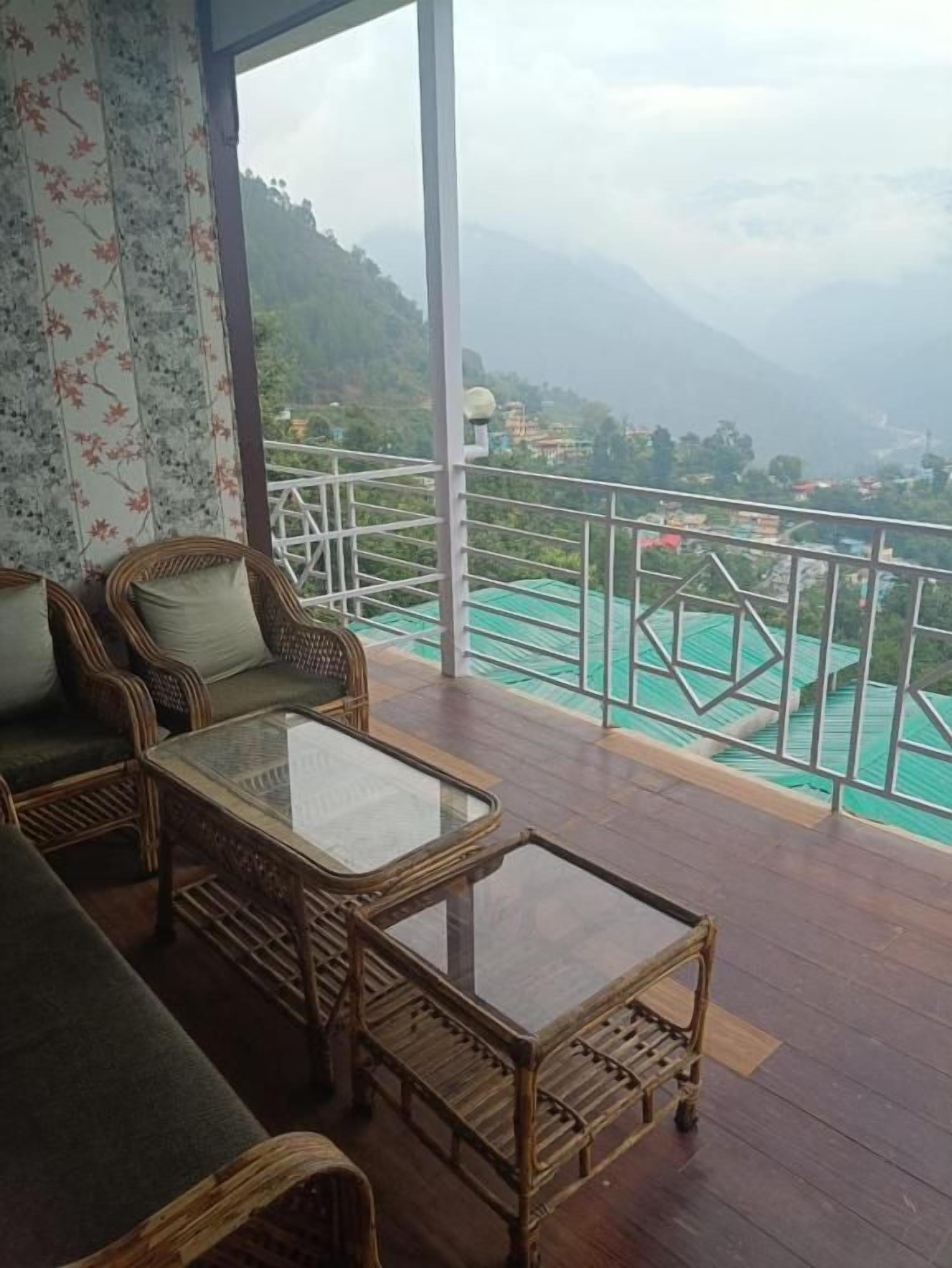 Un balcón con mobiliario de mimbre y una mesa de vidrio, con vista a un paisaje montañoso.