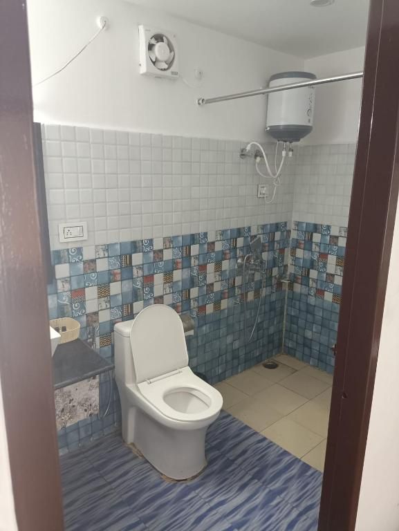 Casa de banho com sanita, chuveiro e parede revestida a azulejos.