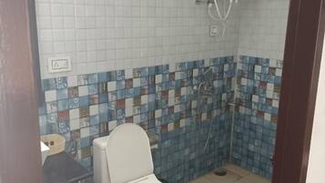Casa de banho com sanita, chuveiro e parede revestida a azulejos.