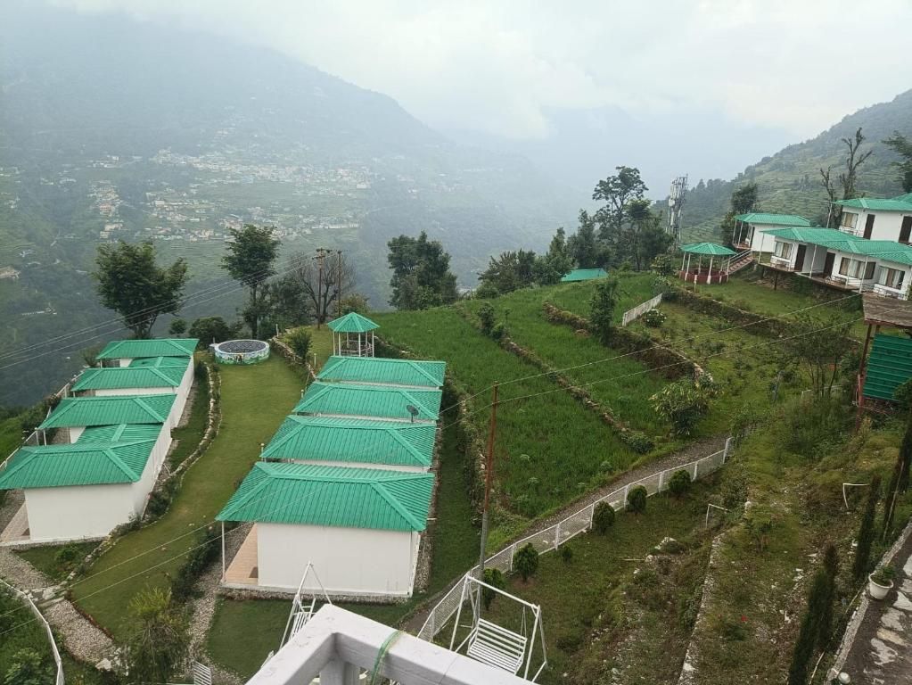 A hillside property with multiple buildings, each with a green roof, surrounded by terraced fields and a mountainous backdrop.