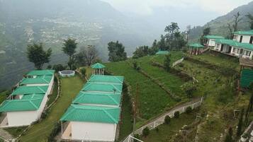 A hillside property with multiple buildings, each with a green roof, surrounded by terraced fields and a mountainous backdrop.