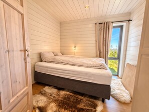 A bedroom with a bed, a nightstand, a window with curtains, and a view of greenery outside. - Geilo ski-in/ski-out, apartment with great views (Hol)