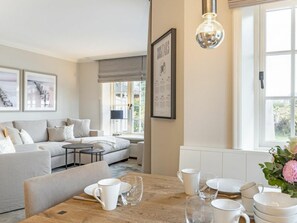 Ein modernes Wohnzimmer mit einer Couch, einem Esstisch mit weißen Tassen und Tellern und einer gerahmten Speisekarte an der Wand.