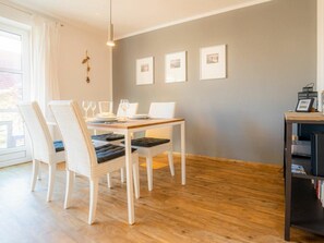 A dining area with a wooden table, white chairs, and a bookshelf. - House Section 30 "sea Lavender" (St. Peter-Ording)