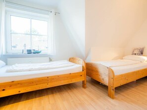 A bedroom with two wooden beds, a window with a view of a building, and a radiator under the window. - House Section 30 "sea Lavender" (St. Peter-Ording)