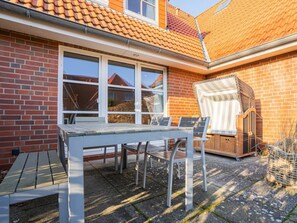 A patio with a table and chairs, a wicker chair, and a small garden area. - House Section 30 "sea Lavender" (St. Peter-Ording)