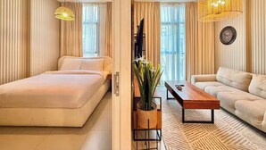 A hotel room with a bed, a sofa, a coffee table, a TV, and a large window with curtains. - Sahab - Golden Hour Almamsha by Alhuty (Sharjah)