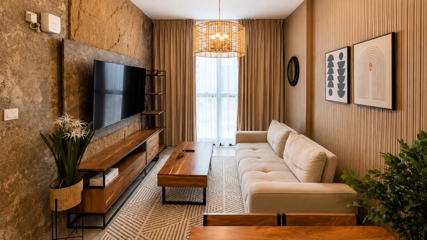 A modern living room with a flat-screen TV, wooden furniture, a woven light fixture, and artwork on the wall. - Sahab - Golden Hour Almamsha by Alhuty (Sharjah)