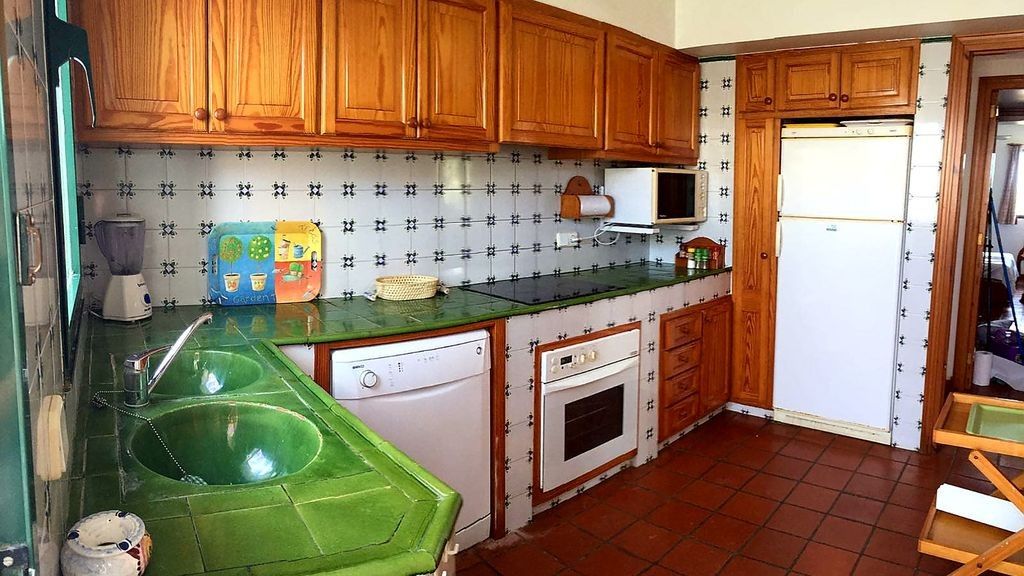 Une cuisine avec des meubles en bois, un évier vert, un four à micro-ondes, un réfrigérateur et un dosseret carrelé.