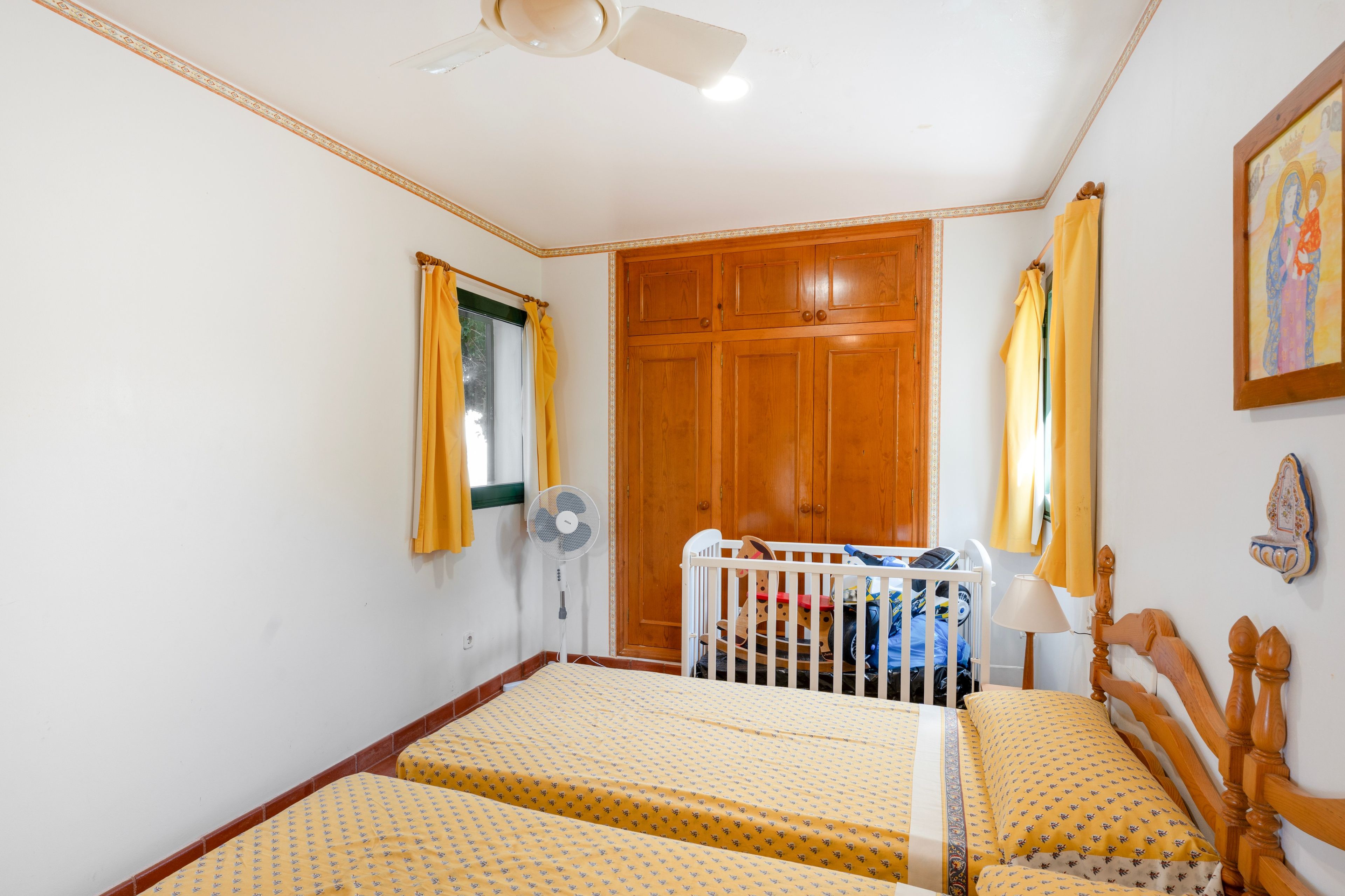 A room with two beds, a wooden wardrobe, a ceiling fan, and a window with curtains.