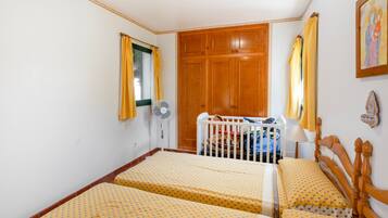 A room with two beds, a wooden wardrobe, a ceiling fan, and a window with curtains.