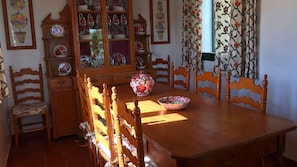 Ein Holzespeisetisch mit Stühlen, eine schrankartige Kommode mit Blumenmuster und ein Fenster mit Vorhängen.