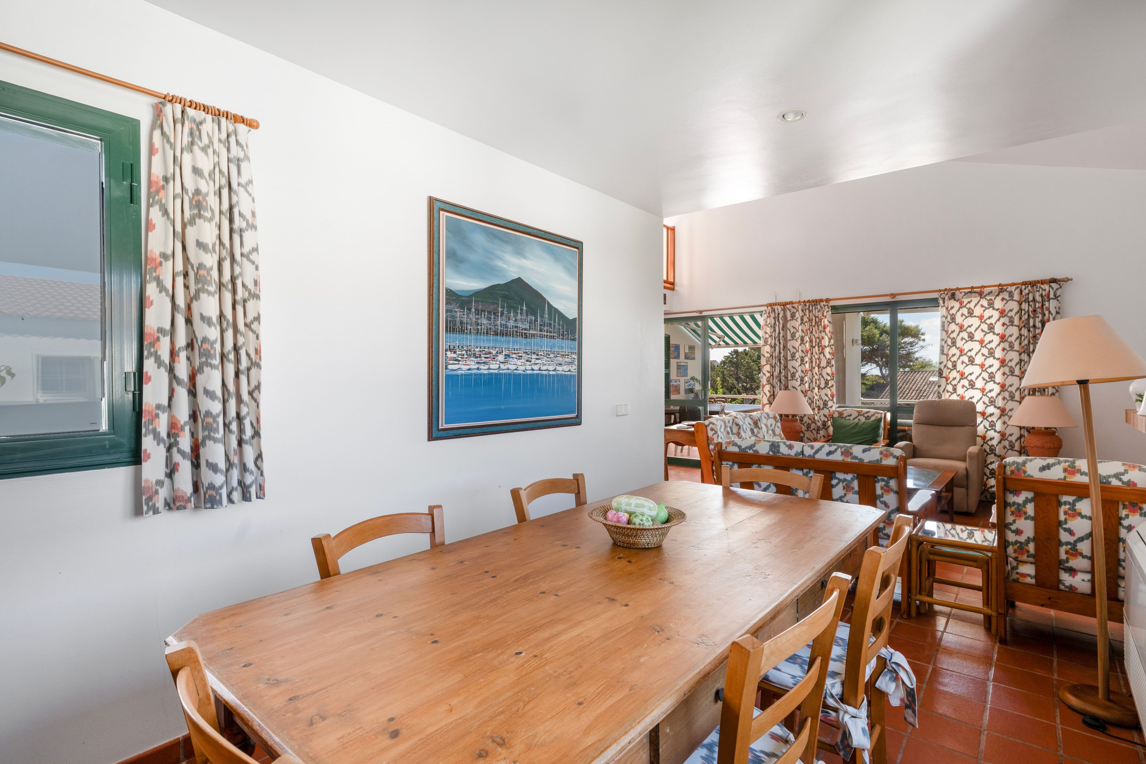 Uma área de refeições com mesa de madeira, cadeiras e um quadro na parede.