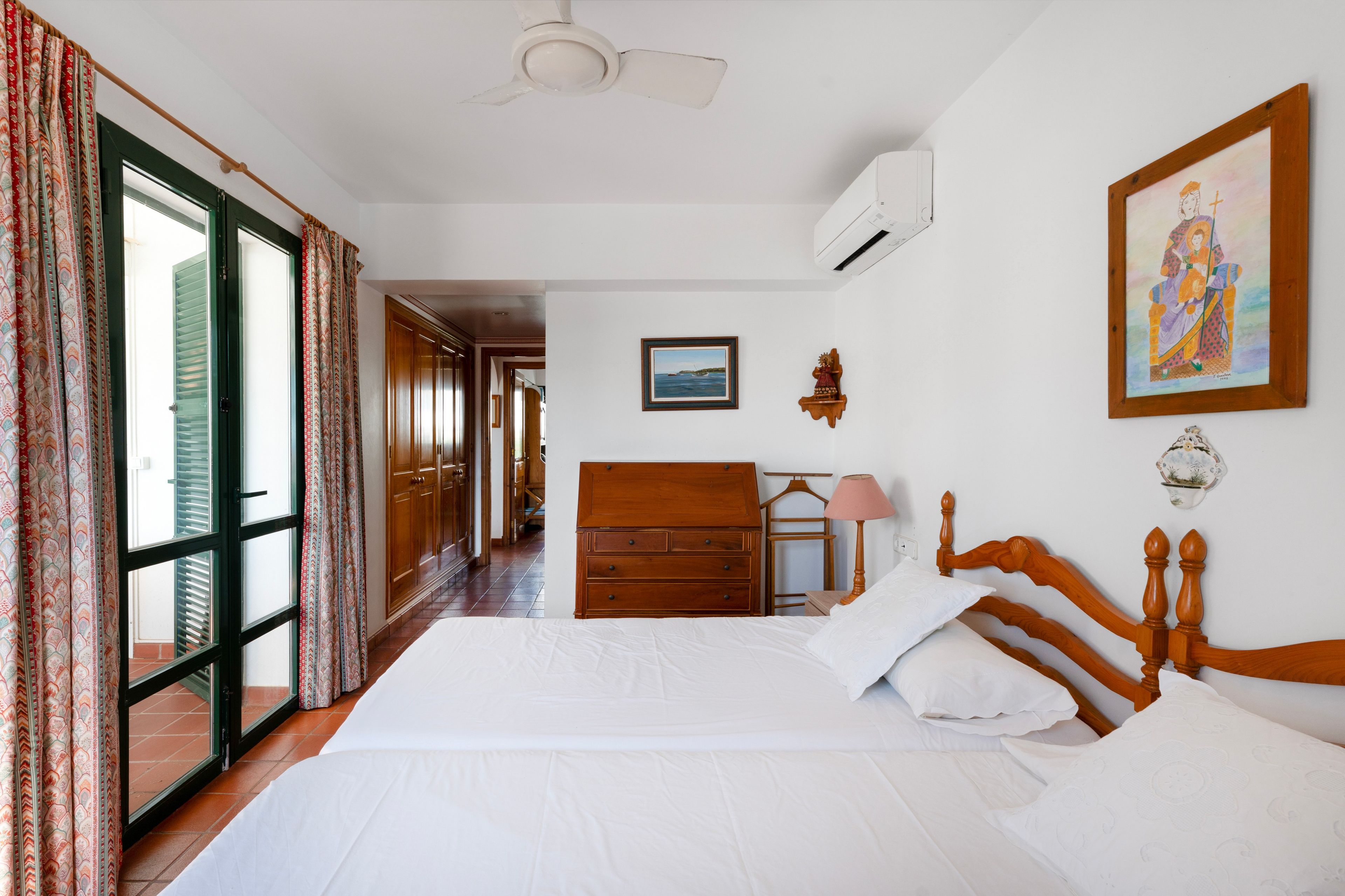 Quarto de hotel com uma cama, penteadeira, pintura e vista para um corredor.