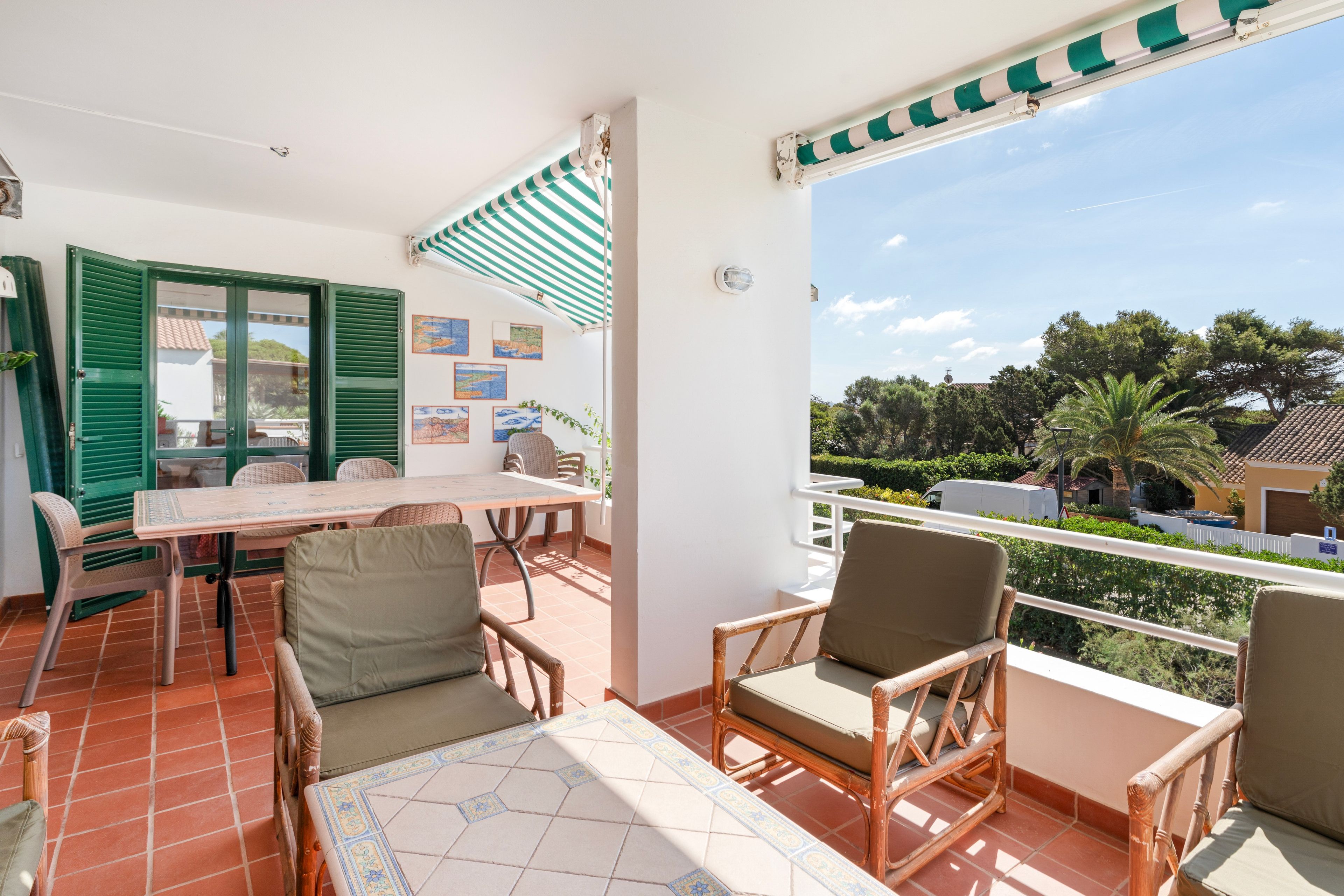 Ein Balkon mit Tisch und Stühlen, Blick auf die Umgebung und ein grün gestreiftes Markisen