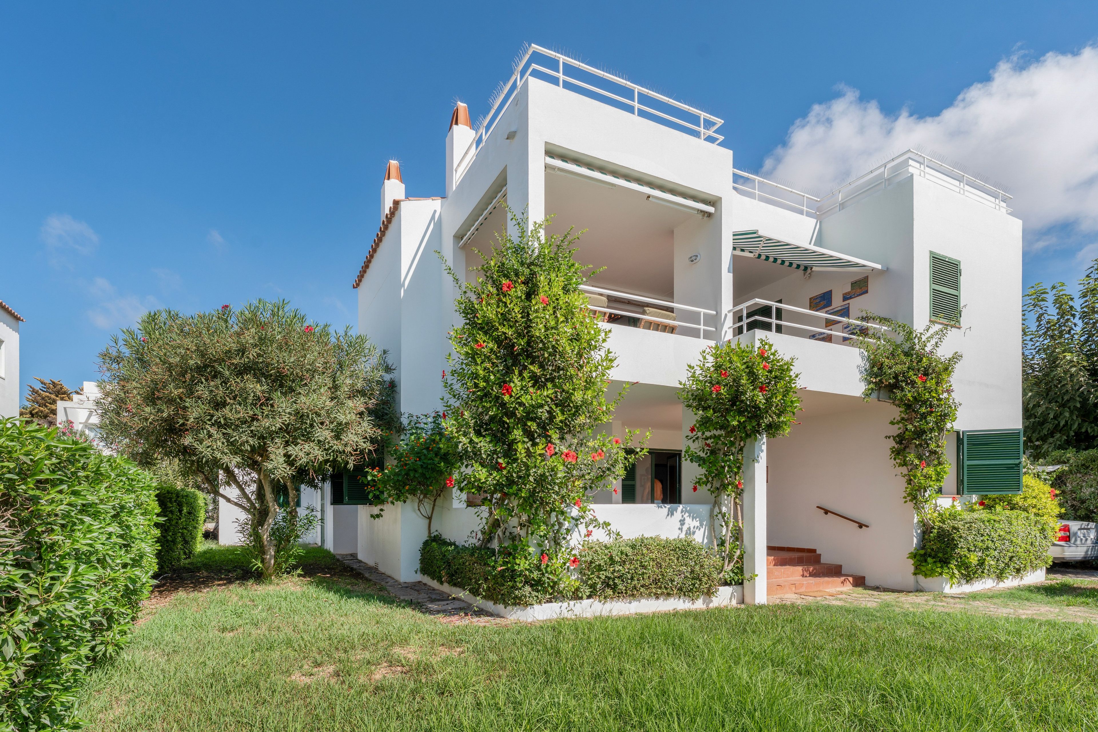 Un bâtiment blanc à deux étages, doté d’un balcon et entouré de verdure et d’arbres.