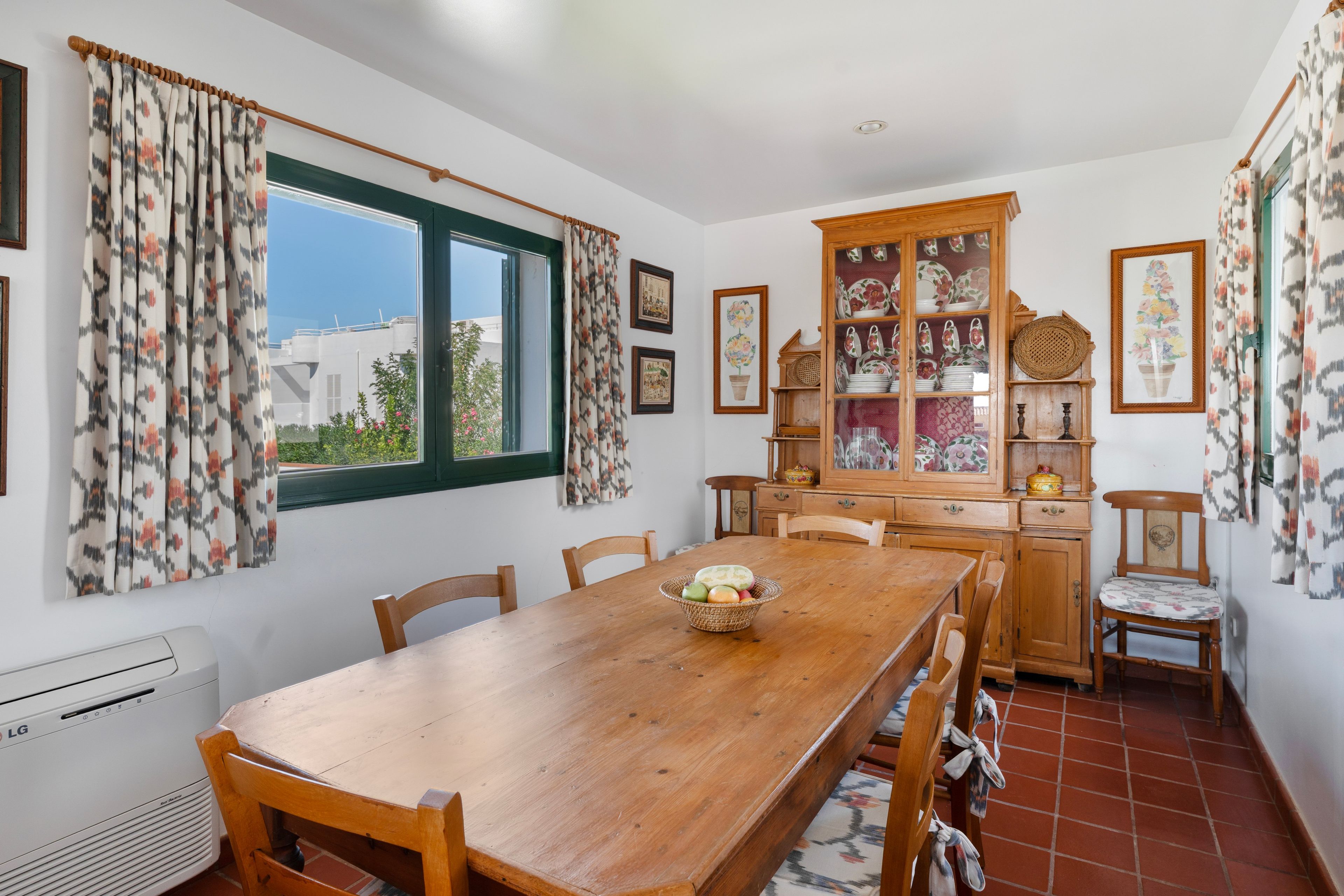 A dining room with a wooden table, chairs, a cabinet with glass doors, and a window with curtains.