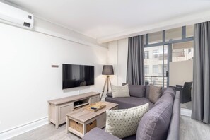 A modern living room with a flat-screen TV, a sofa, a coffee table, and a lamp. - Serene 1-bedroom apartment with AC in vibrant Cape Town (Cape Town)