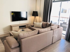 A modern living room with a large flat-screen TV, a floor lamp, and a sofa set. - Serene 1-bedroom apartment with AC in vibrant Cape Town (Cape Town)