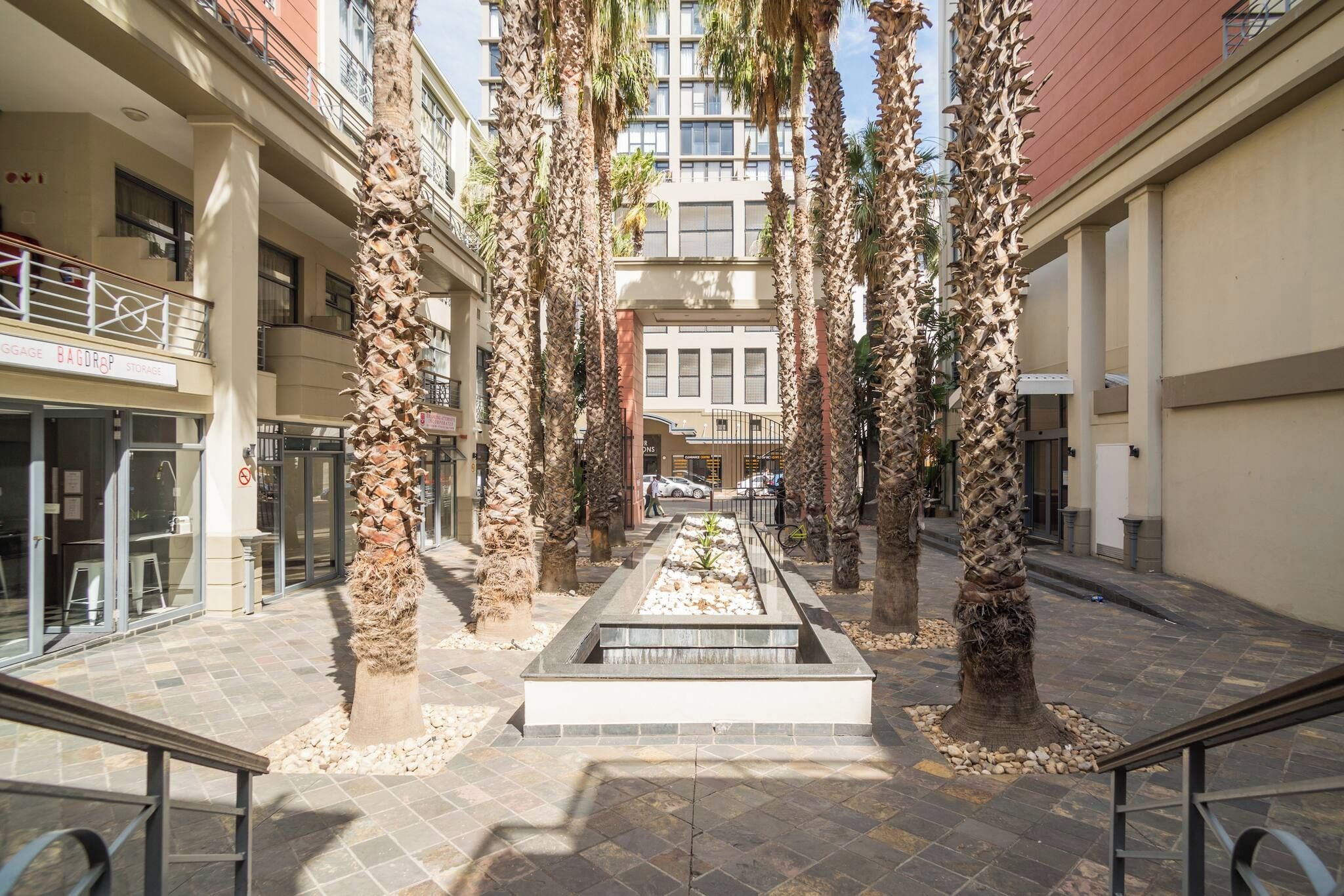 A courtyard with palm trees, a central water feature, and a building with multiple floors and balconies.