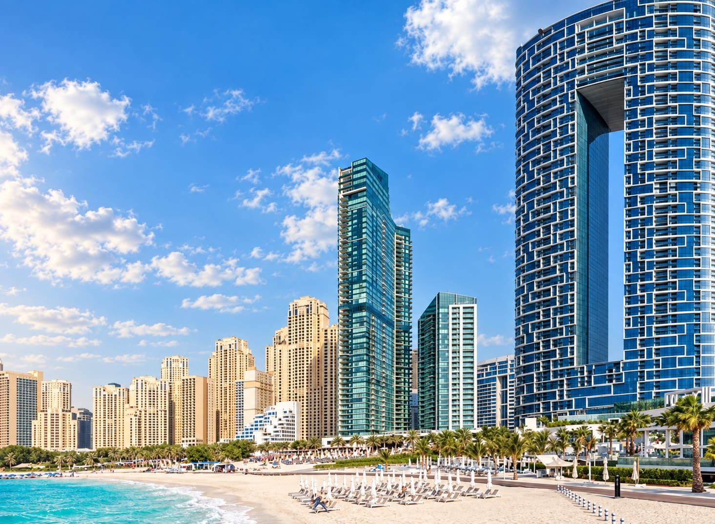 Un paysage urbain côtier avec des immeubles modernes de grande hauteur, une plage avec des transats et un ciel bleu dégagé.