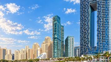 Un paysage urbain côtier avec des immeubles modernes de grande hauteur, une plage avec des transats et un ciel bleu dégagé.