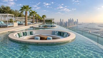 Una piscina infinita lujosa con zonas de estar y palmeras, con vista a un horizonte urbano.