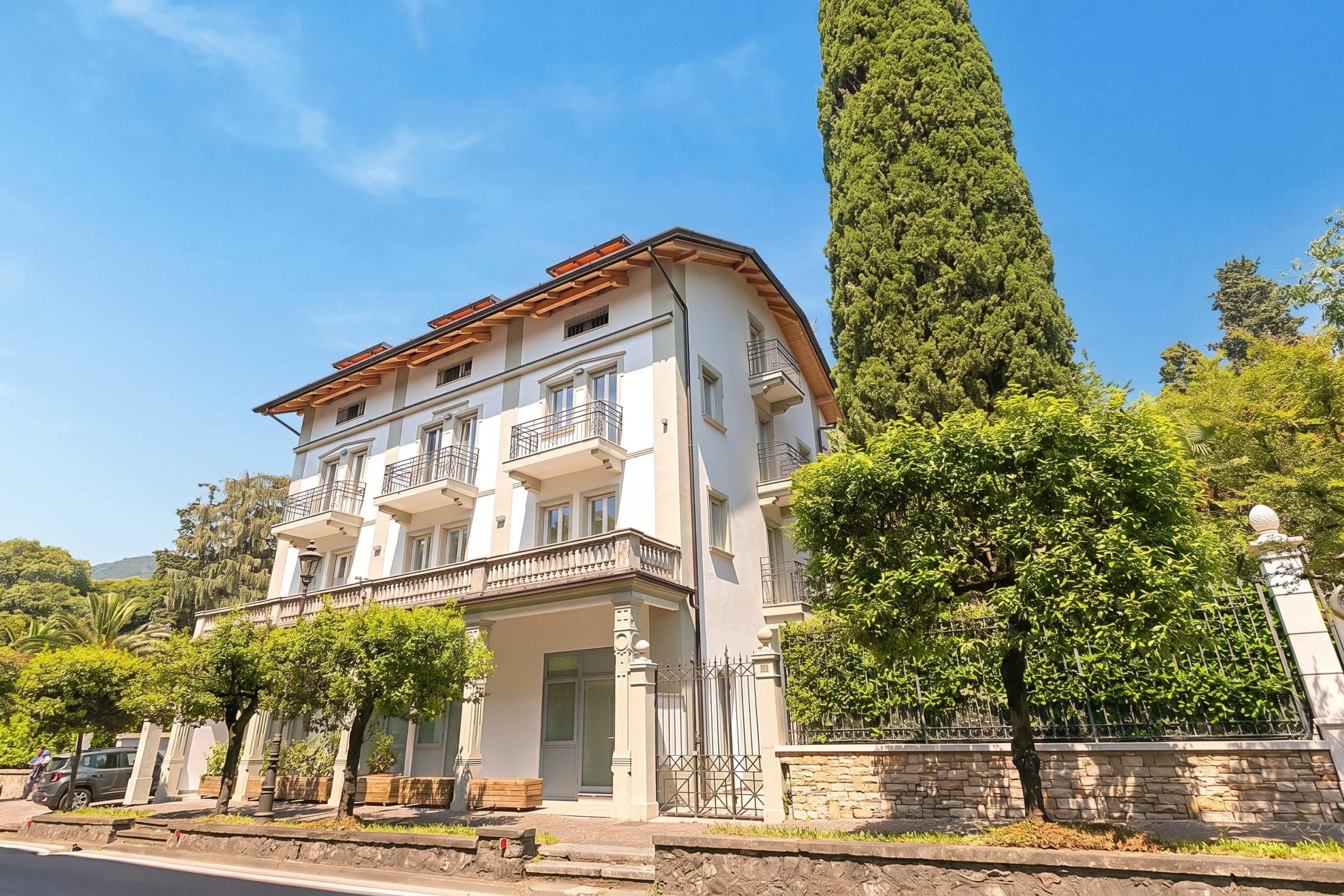 Un edificio de varios pisos con balcones, fachada de piedra y un árbol alto al frente.