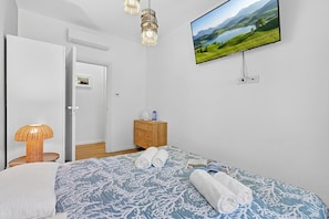 A bedroom with a bed, a television mounted on the wall, a wooden dresser, and a door leading to another room. - Kamy Home Steps to the Lake & Free Park (Gardone Riviera)