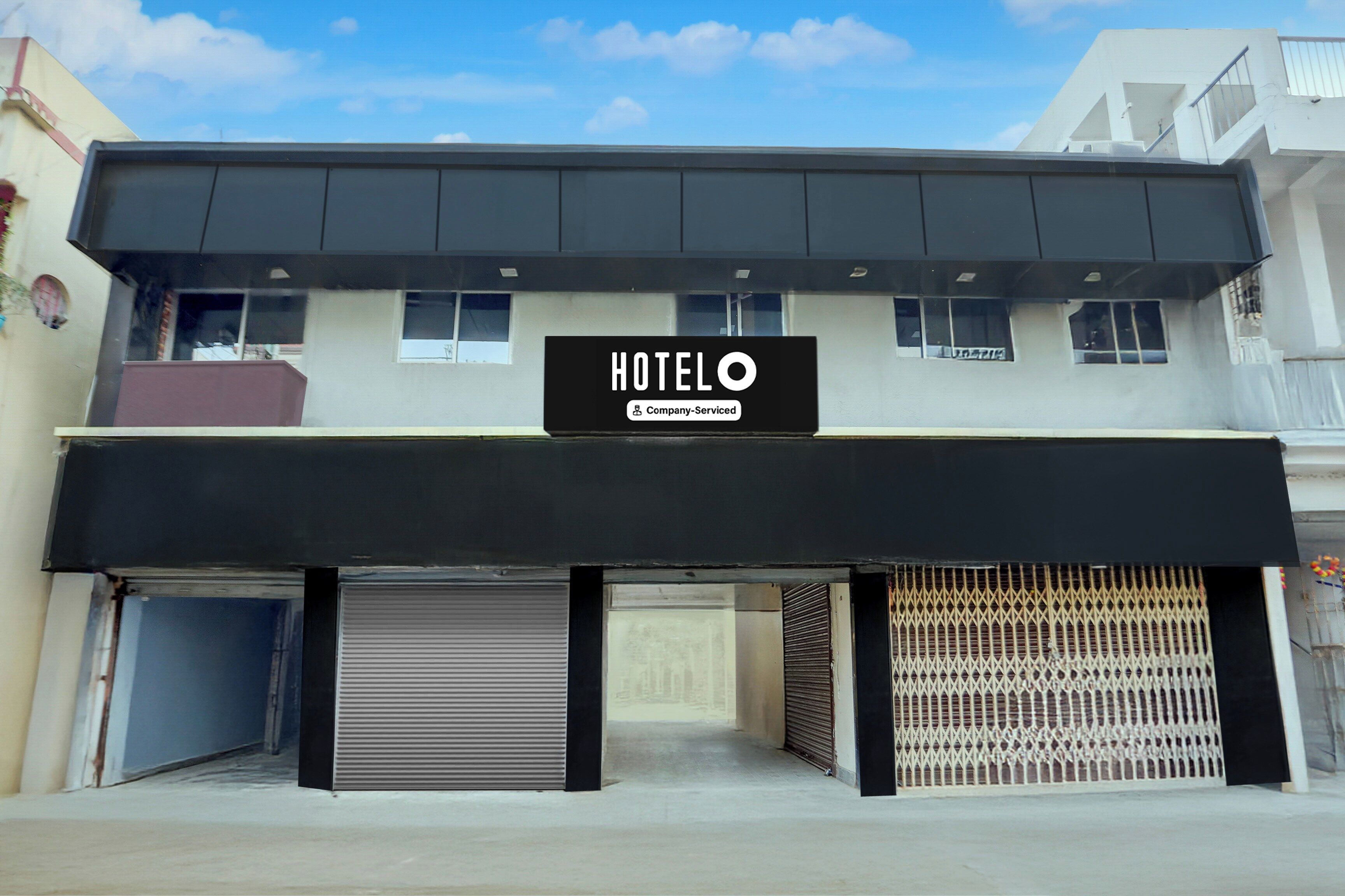 A hotel with a sign indicating it is company-serviced. There are closed shutters on the ground floor, and the building has a flat roof.