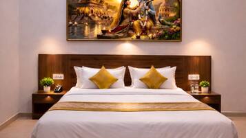 A bedroom with a large bed, a ceiling fan, an air conditioning unit, a nightstand with a phone and a plant, and a painting above the bed.