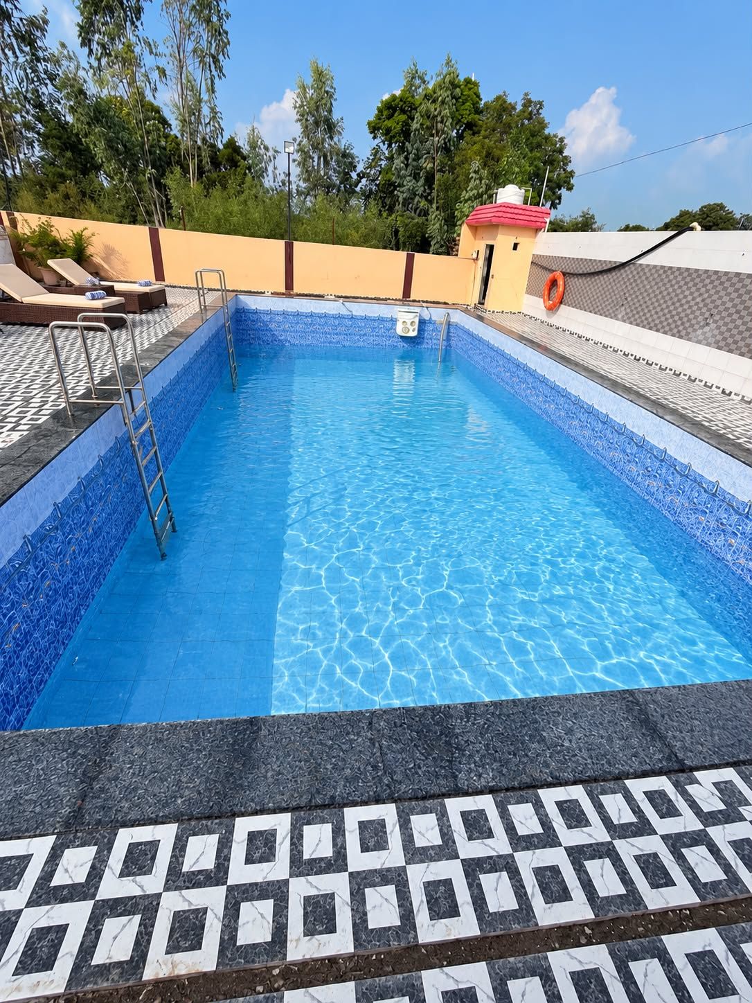 Una piscina rectangular con revestimiento de azulejos azules, rodeada por una terraza también de azulejos con un diseño geométrico.