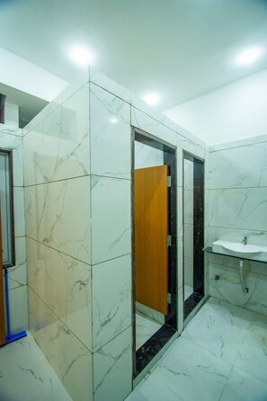 A bathroom with white marble tiles, a wooden door, and a glass partition.