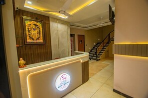 A hotel reception area with a reception desk, a staircase, and a wall-mounted artwork.