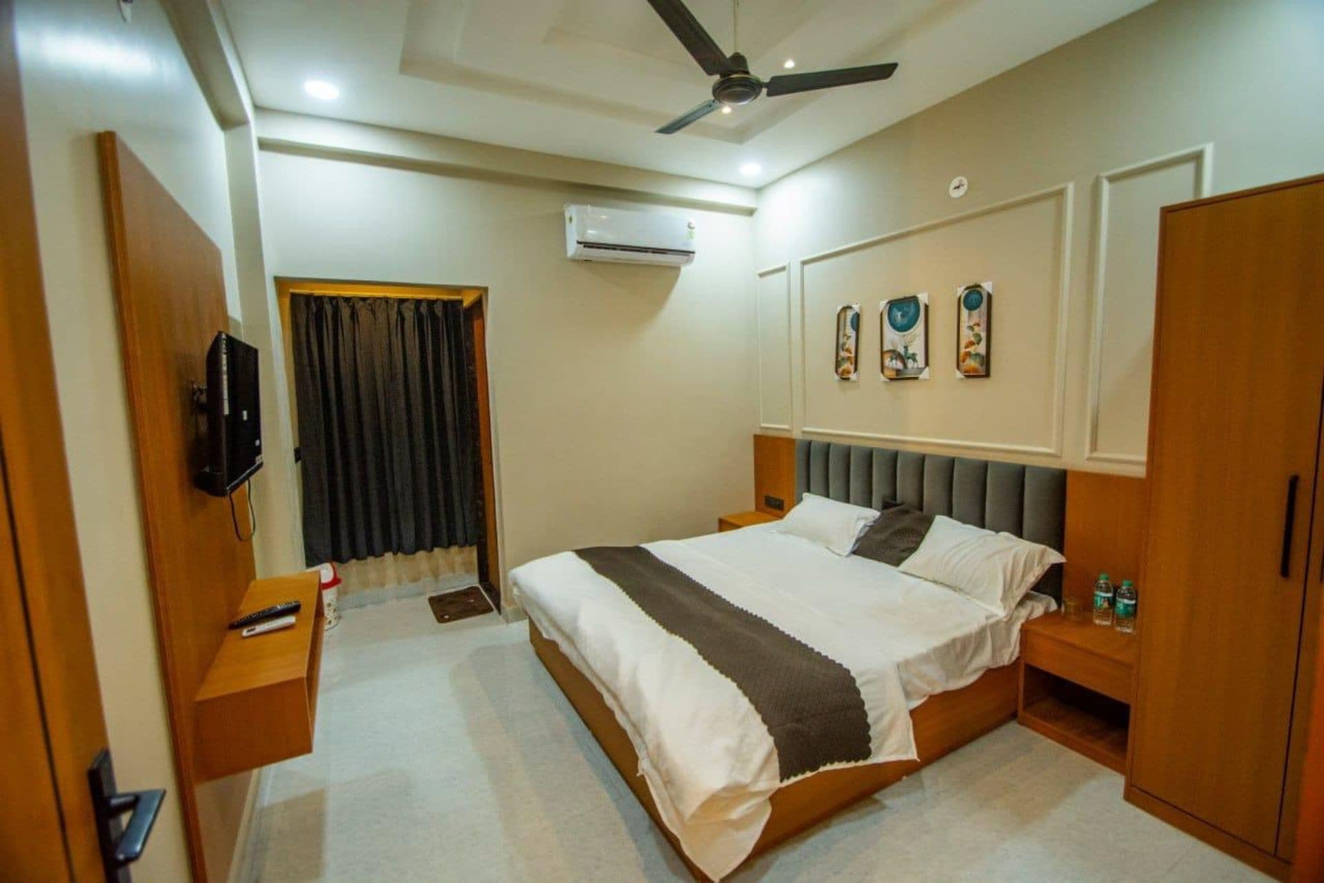Una habitación de hotel con cama, mesitas de noche, armario, ventilador de techo y aire acondicionado.