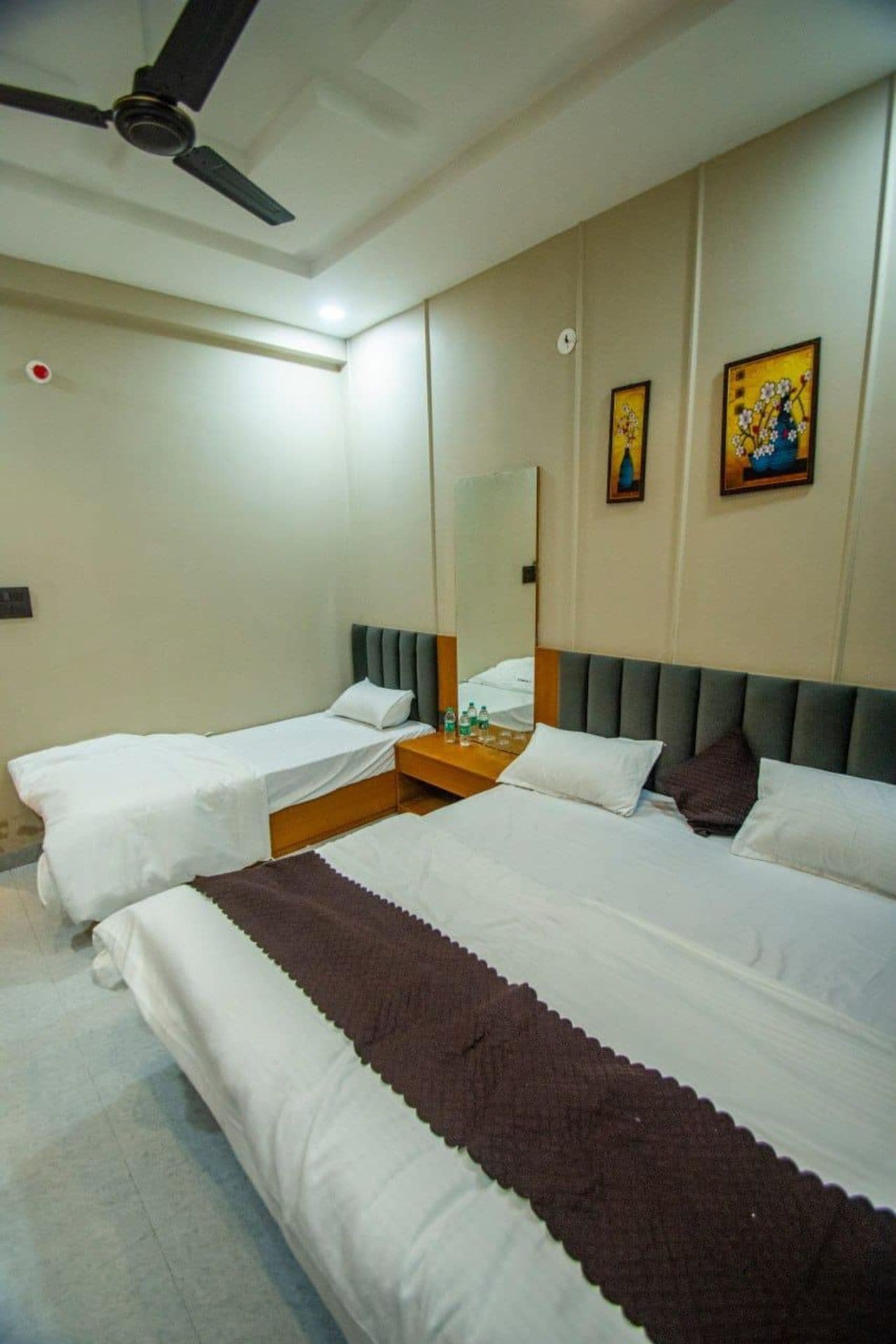 Habitación de hotel con dos camas, un ventilador de techo, un espejo y obras de arte en la pared.