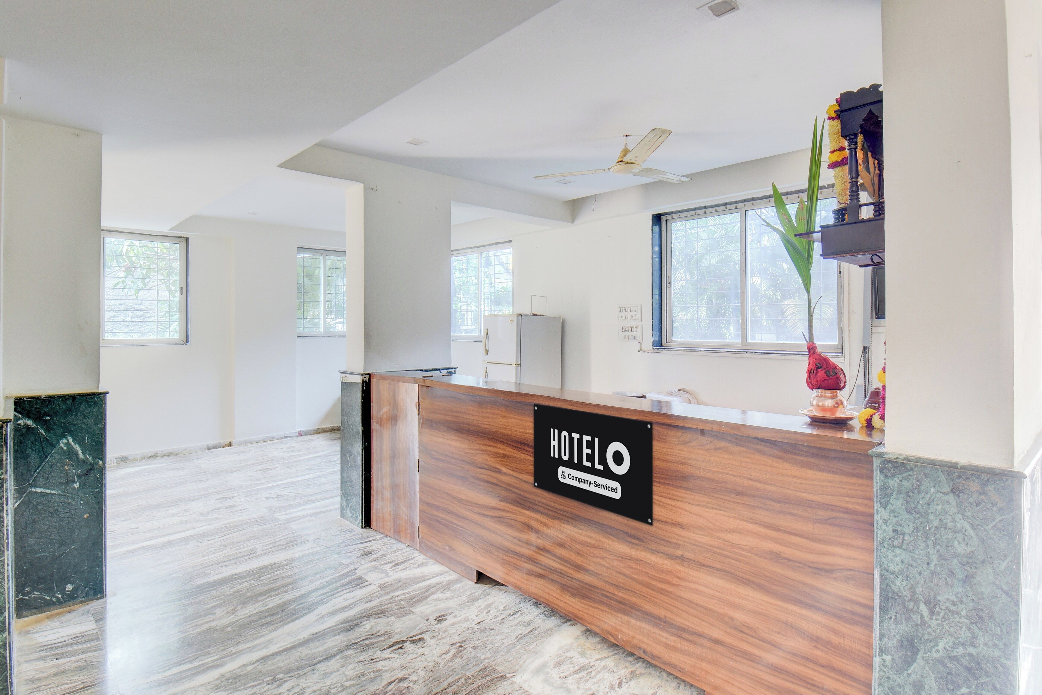 A hotel reception area with a wooden reception desk, a sign indicating it's a company-serviced hotel, and a view of the interior.