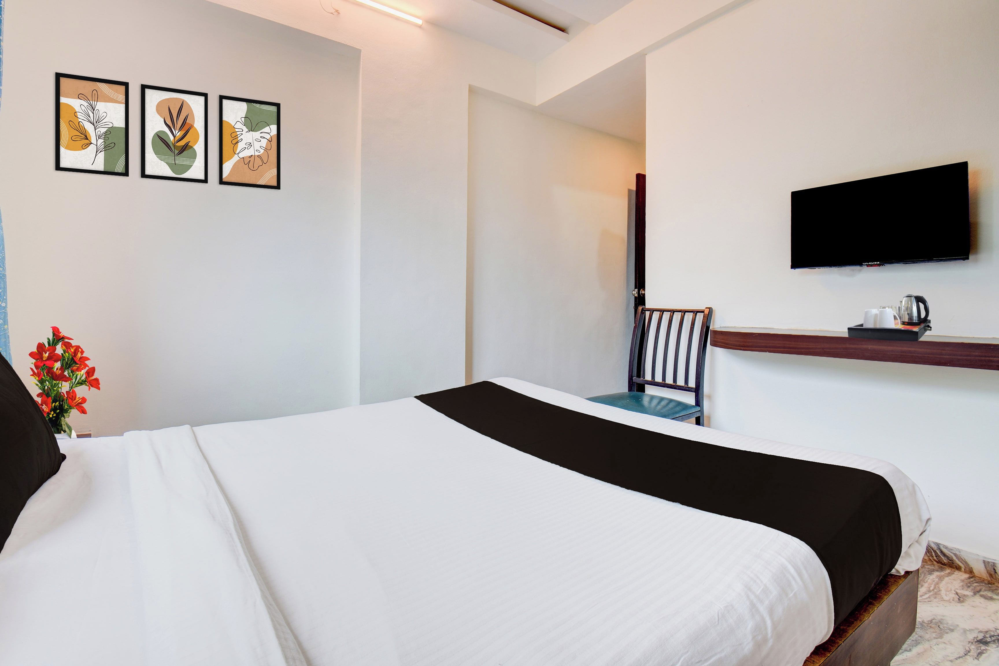 Une chambre d’hôtel équipée d’un lit, d’un téléviseur à écran plat fixé au mur et d’une petite table avec une bouilloire et des tasses.