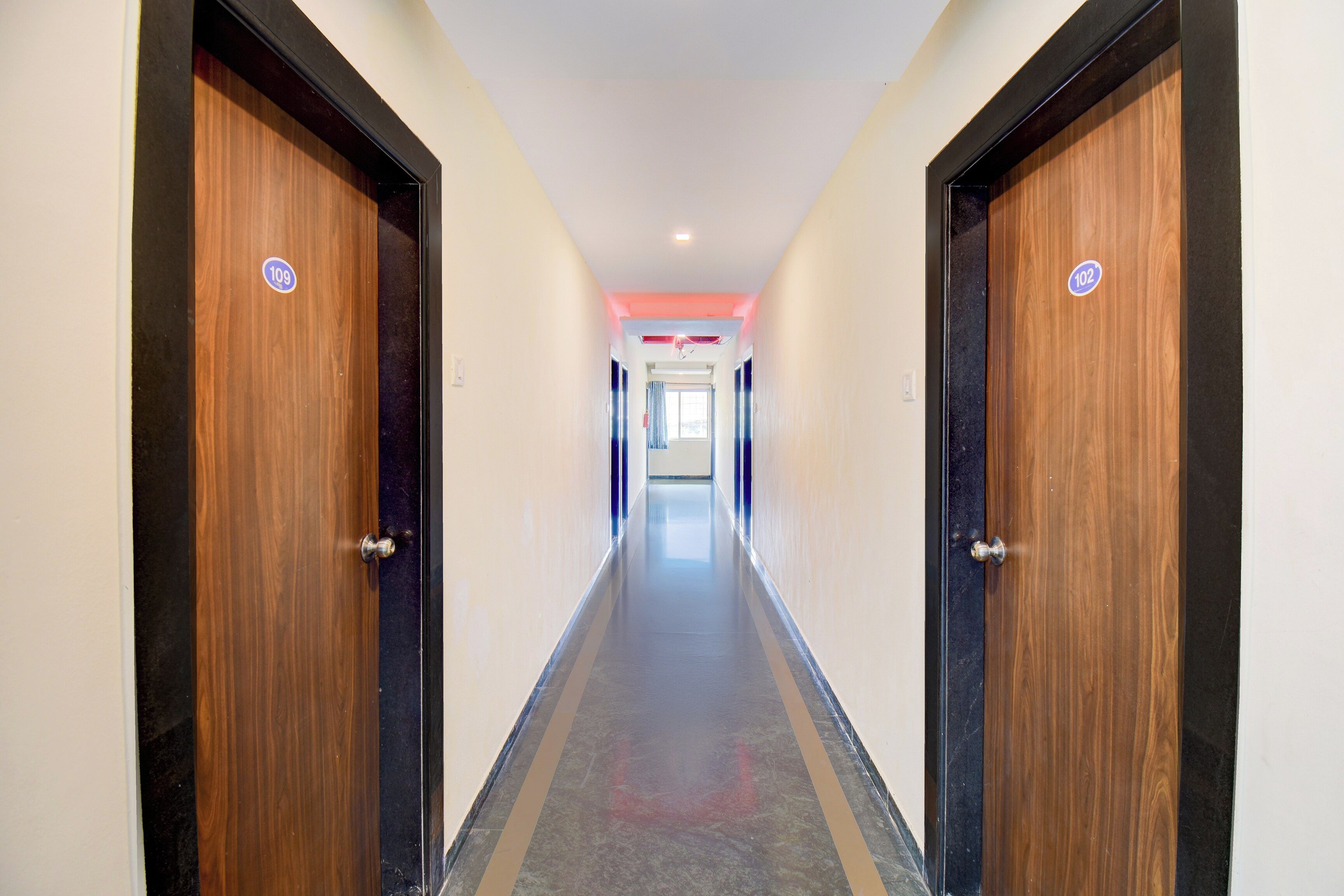 Un couloir avec deux portes de chaque côté, menant à une pièce dont une fenêtre se trouve au fond.