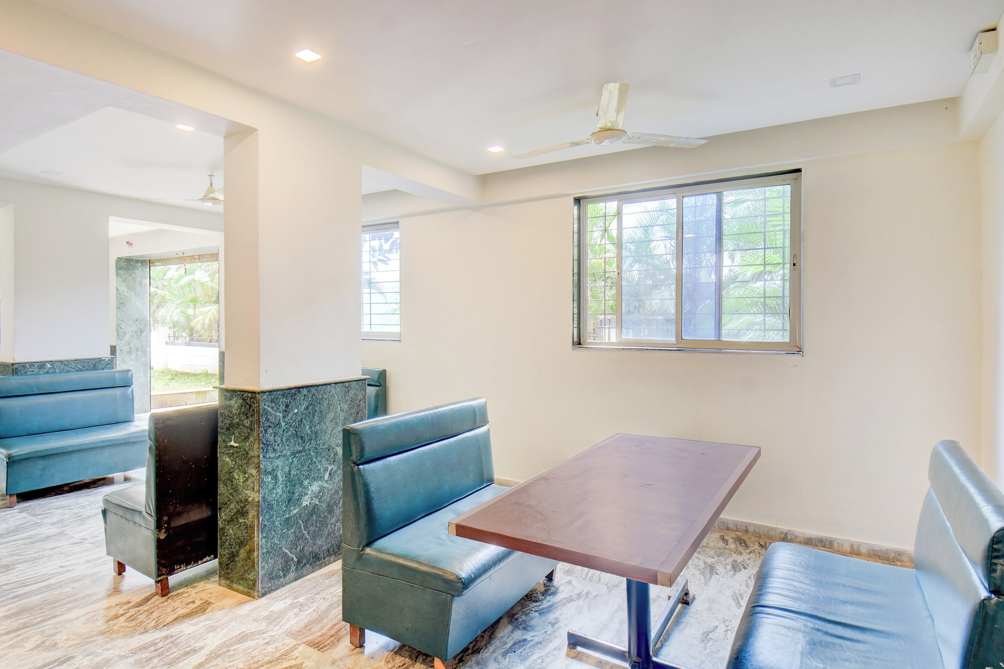 Una habitación con una mesa y bancos, un ventilador de techo y una ventana con vistas a zonas verdes.