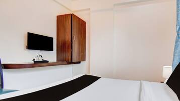 A hotel room with a bed, a television mounted on the wall, a wooden wardrobe, and a bedside table with a tray of items.