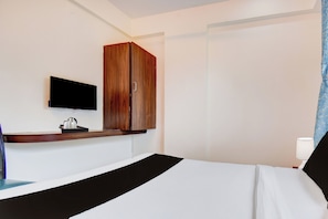 A hotel room with a bed, a television mounted on the wall, a wooden wardrobe, and a bedside table with a tray of items.