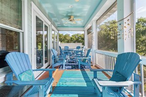 Eine überdachte Veranda mit blauen Adirondack-Stühlen, einem Deckenventilator und Blick ins Freie.