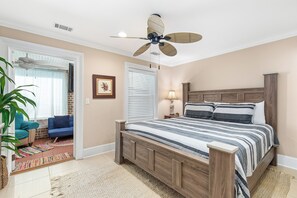 Ein Schlafzimmer mit einem Holzbett, einem Deckenventilator, einem Nachttisch, einer Lampe und Blick ins Freie.