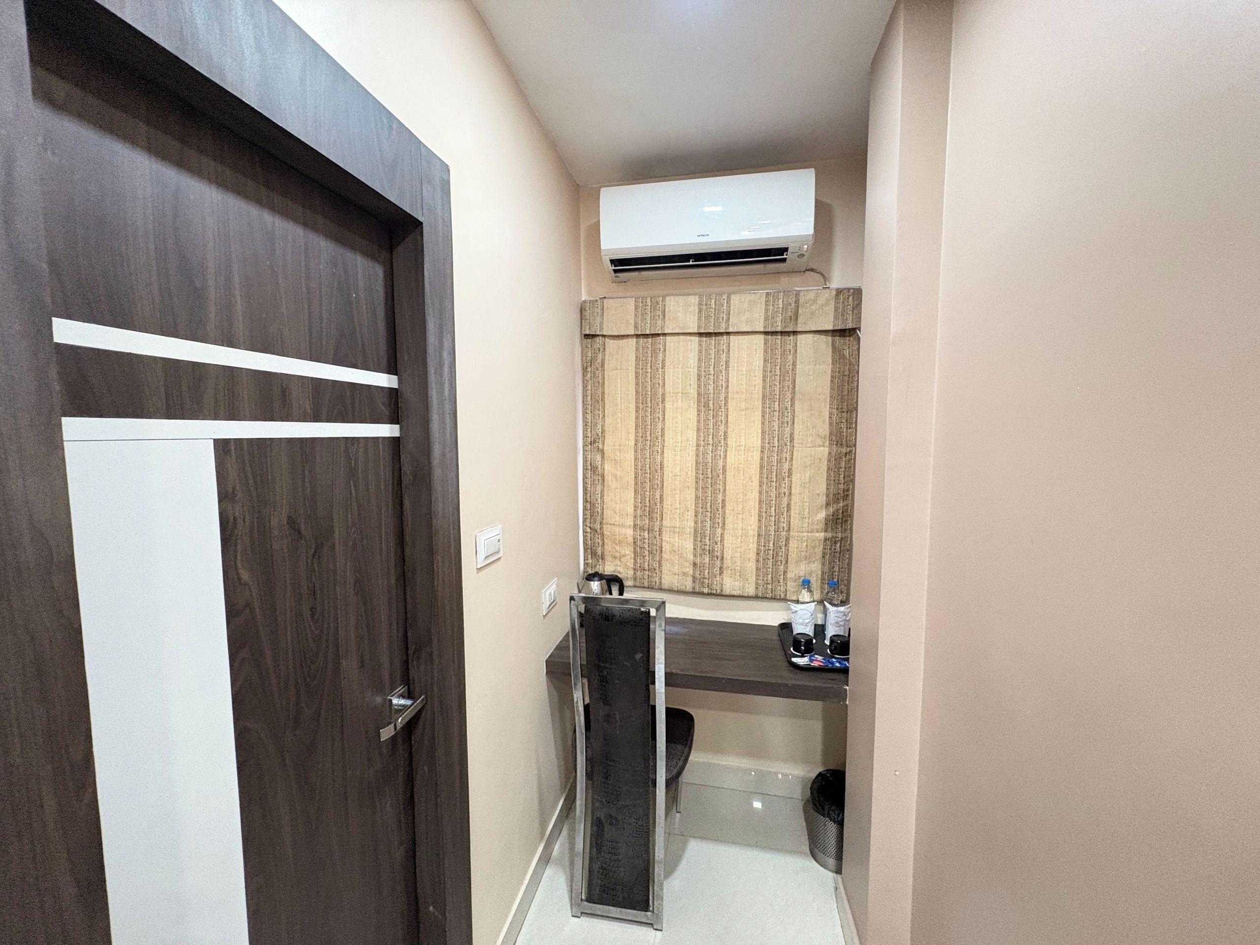 Un pasillo estrecho con una puerta de madera, una pequeña kitchenette con mostrador y un equipo de aire acondicionado montado en la pared.