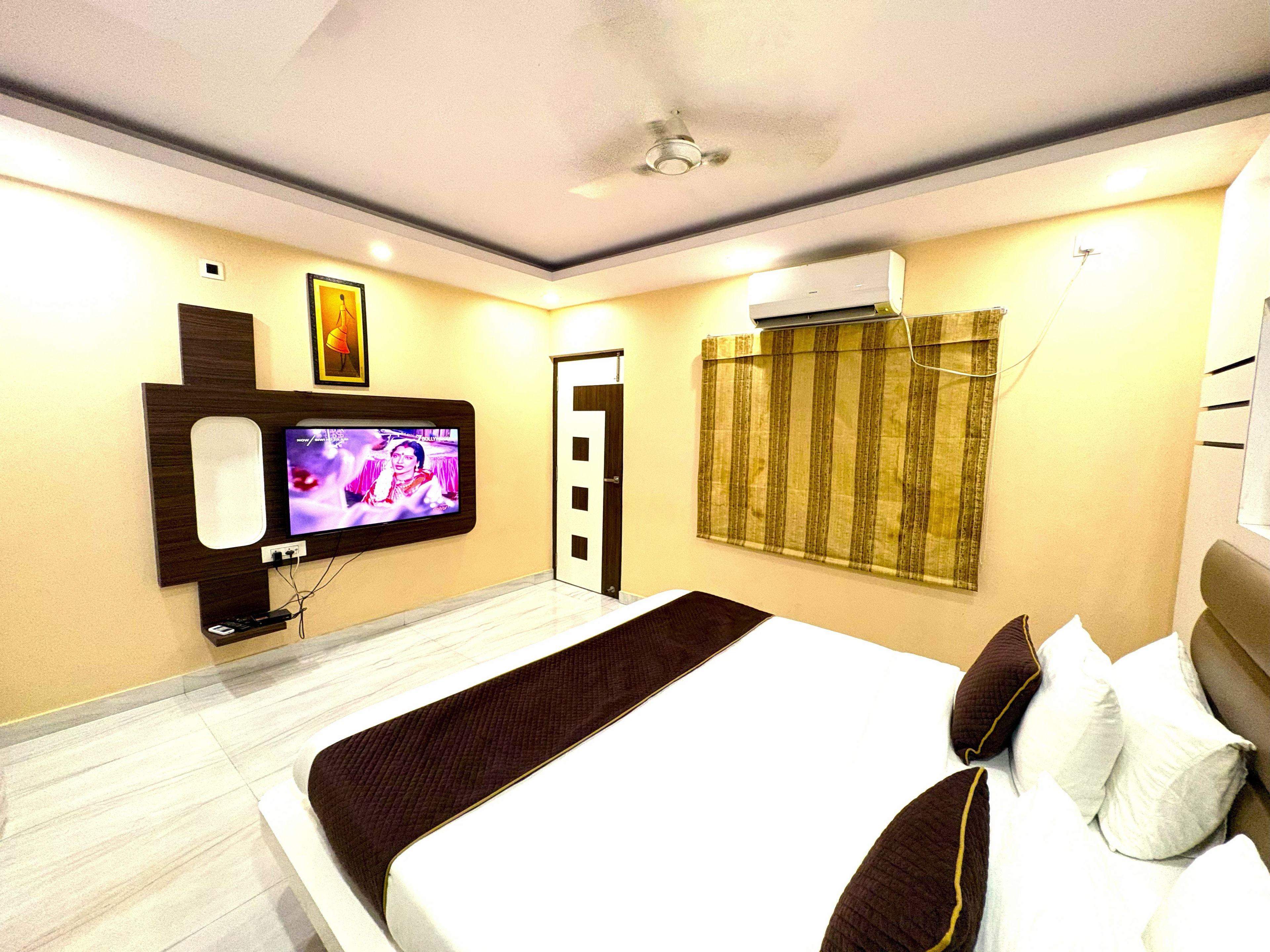 Habitación de hotel con cama, televisor montado en la pared, aire acondicionado y una puerta con cortina.