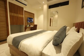 Quarto de hotel com cama, escrivaninha, televisão e espelho.